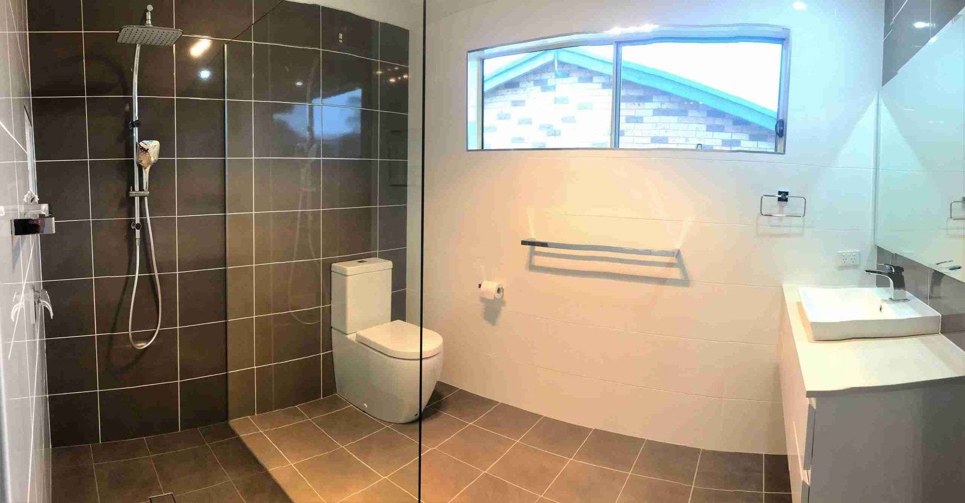Modern bathroom with walk-in shower, toilet, sink, towel rack, and a small window.