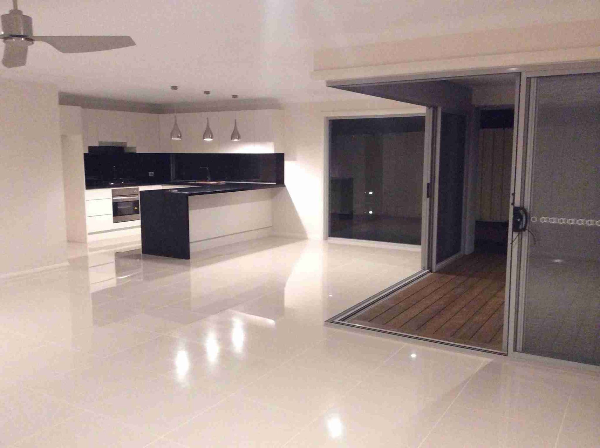 Modern open-plan kitchen and living area with glossy white floors, black cabinets, and a covered patio opening.