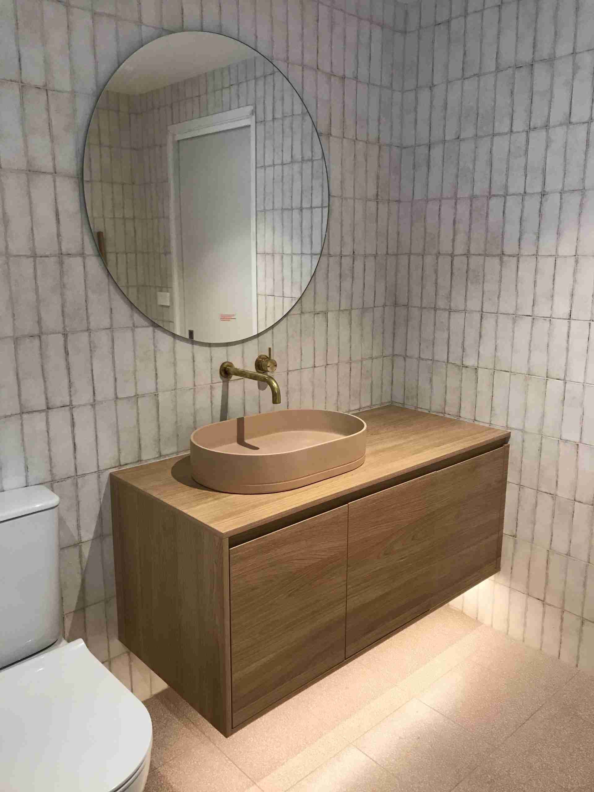 Modern bathroom vanity with round mirror, wood cabinet, and tiled walls