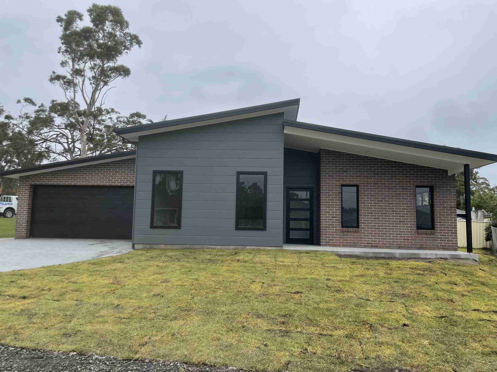 Modern gray single-story house with brick accents, a garage, and a front lawn under an overcast sky