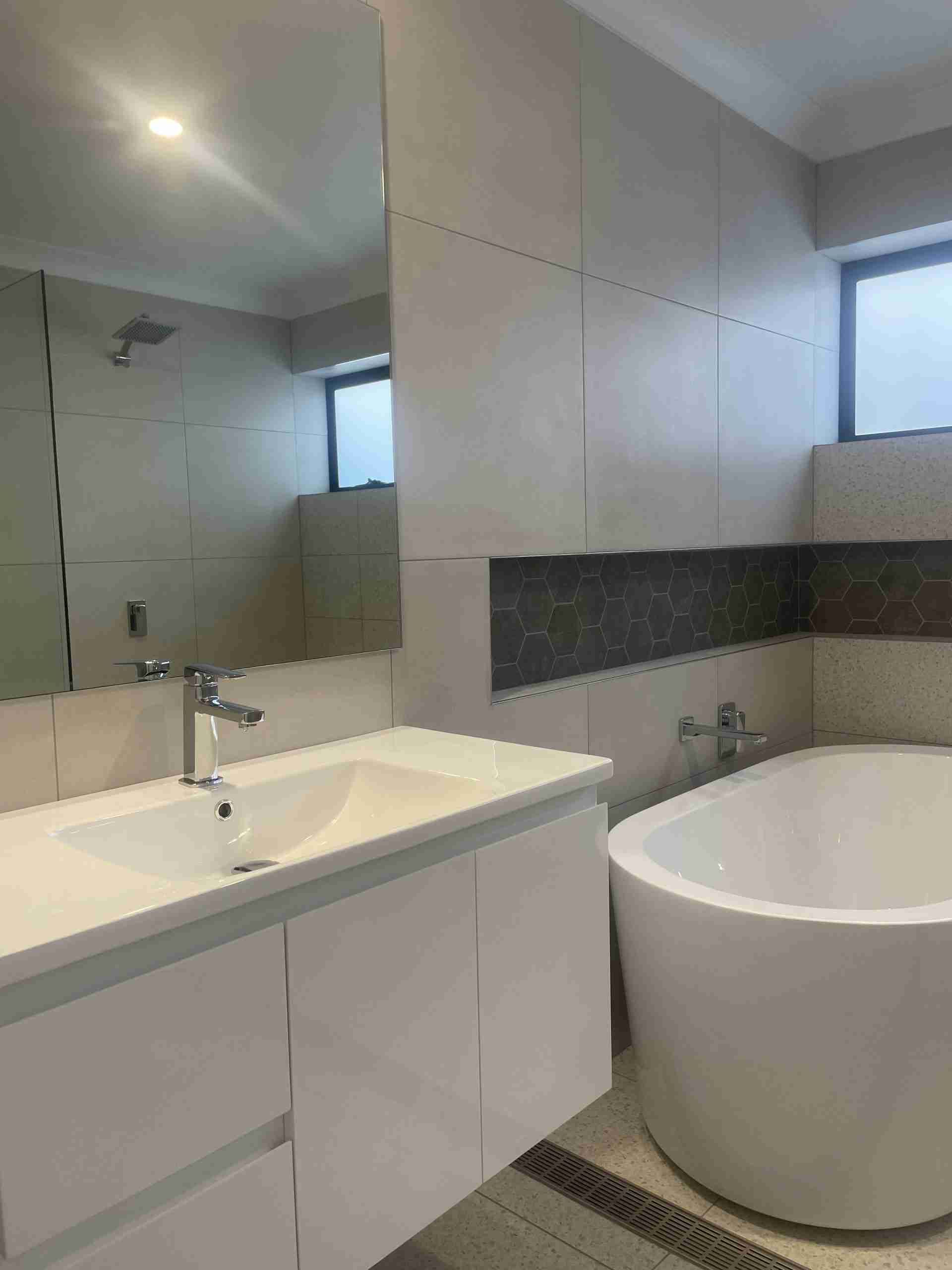 Modern bathroom with a white sink, large mirror, and round bathtub with tiled walls