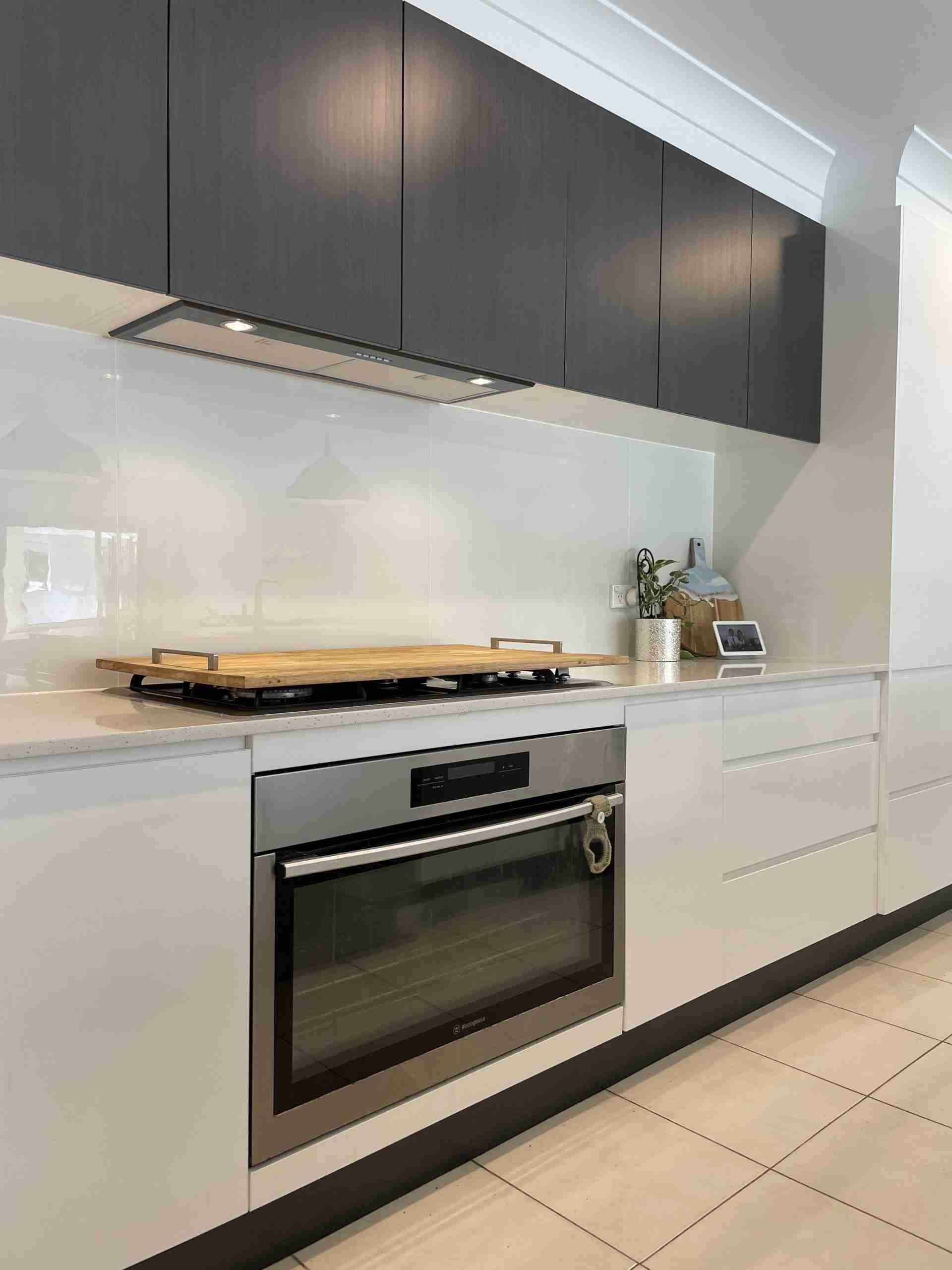 Modern kitchen with dark cabinets, white countertops, built-in oven, and tiled floor.