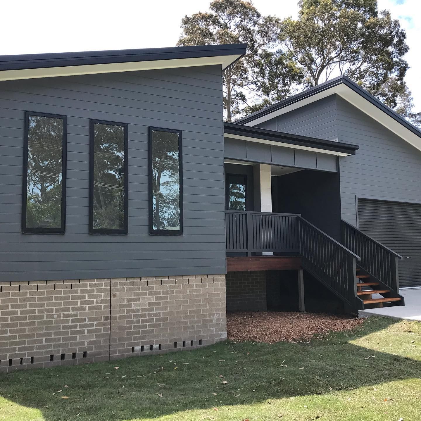 Gray brick house with dark trim, tall windows, and a small front porch with stairs.