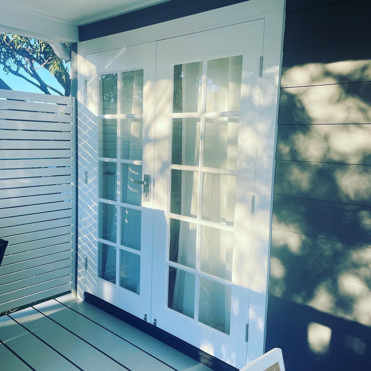 White French doors with glass panes beside a white slatted fence on a sunlit patio