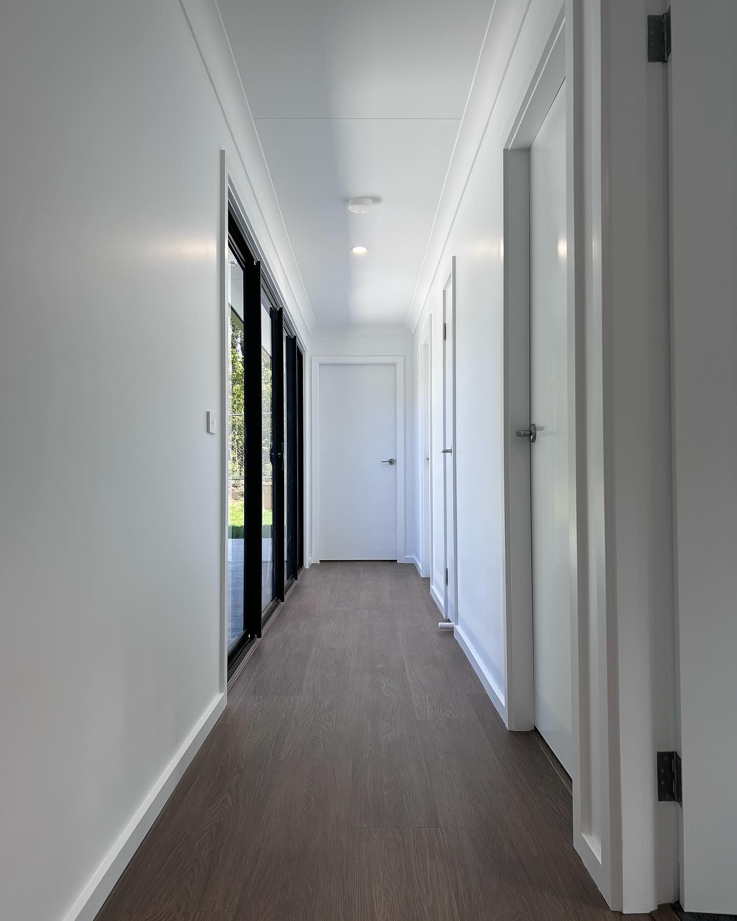 Narrow white hallway with brown carpet and large windows on the left.