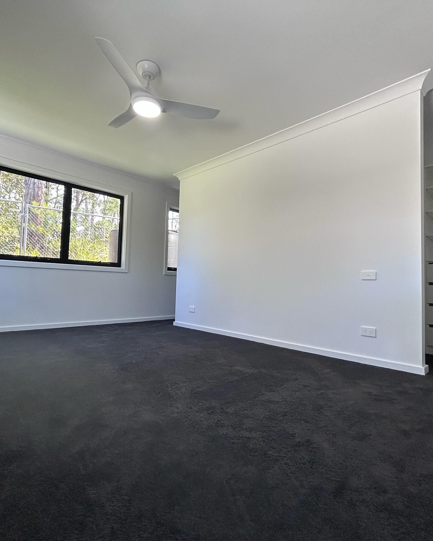 Empty unfurnished room with dark carpet, white walls, a ceiling fan, and a window.