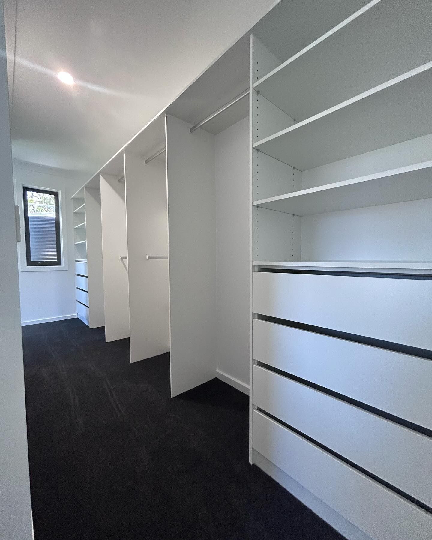 Empty walk-in closet with white shelving and hanging rods beside a dark carpeted floor.