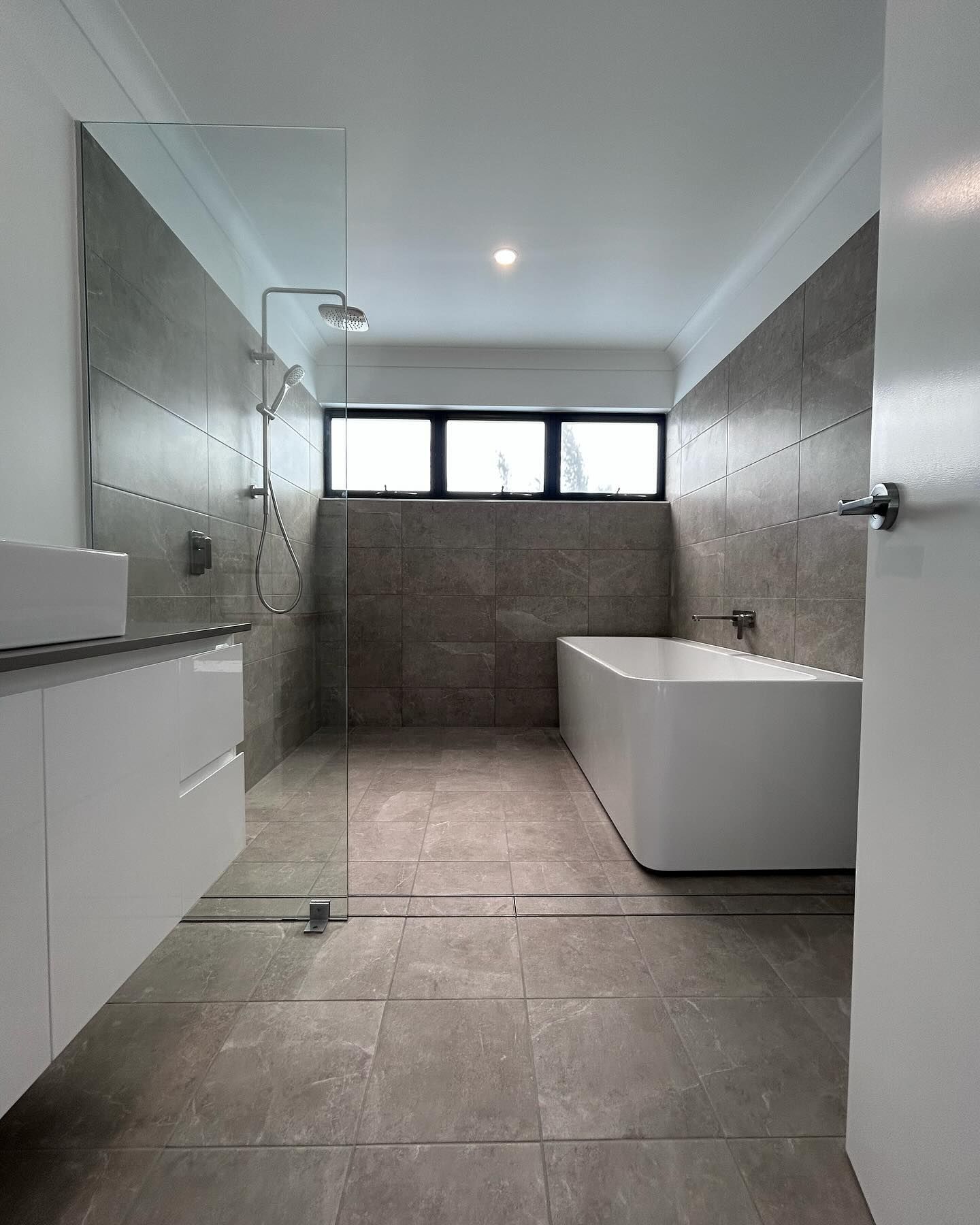 Modern bathroom with walk-in shower, freestanding tub, and gray tiled walls and floor.