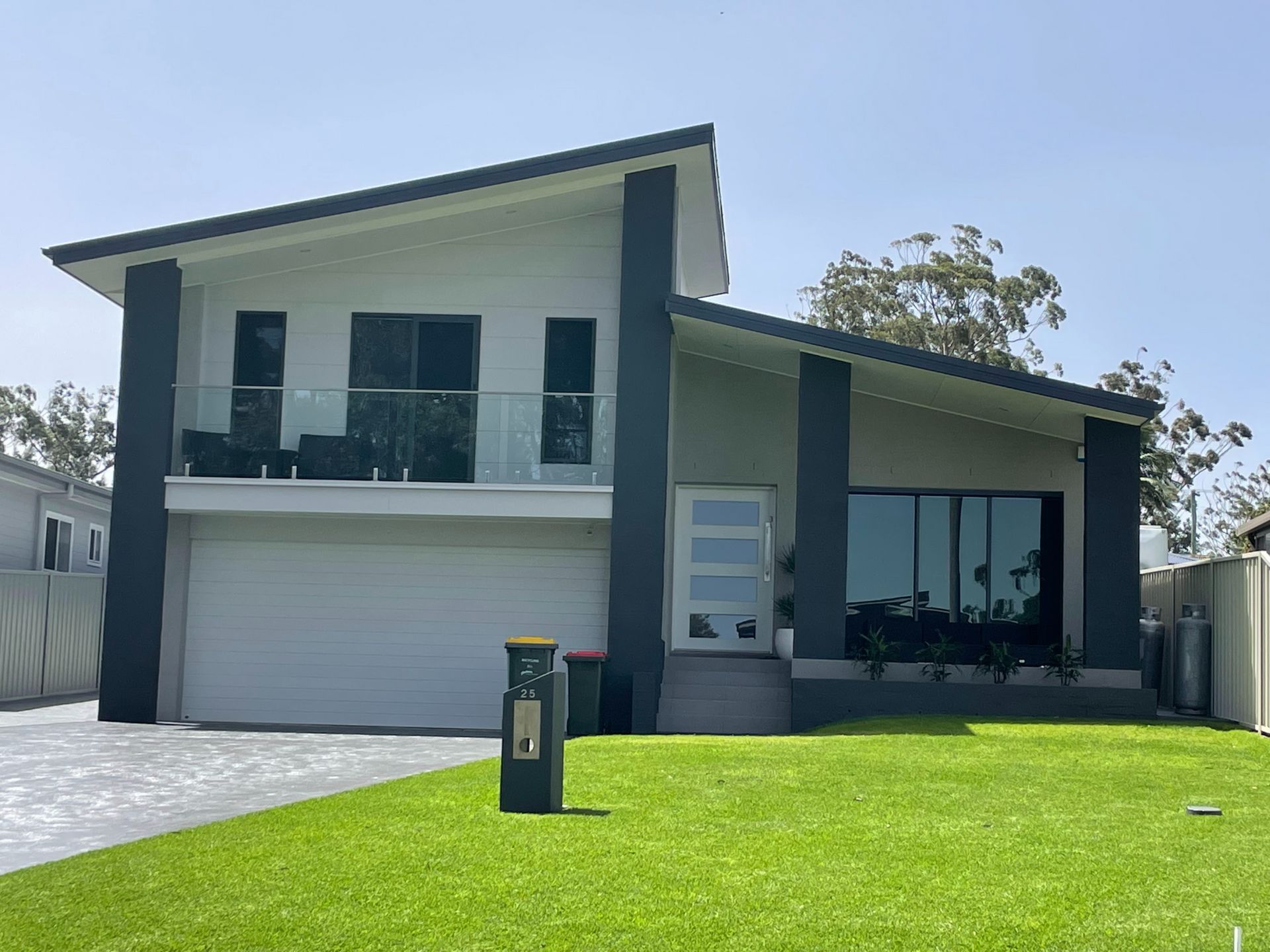 Two-story modern house with white garage, dark accents, and a green lawn in front