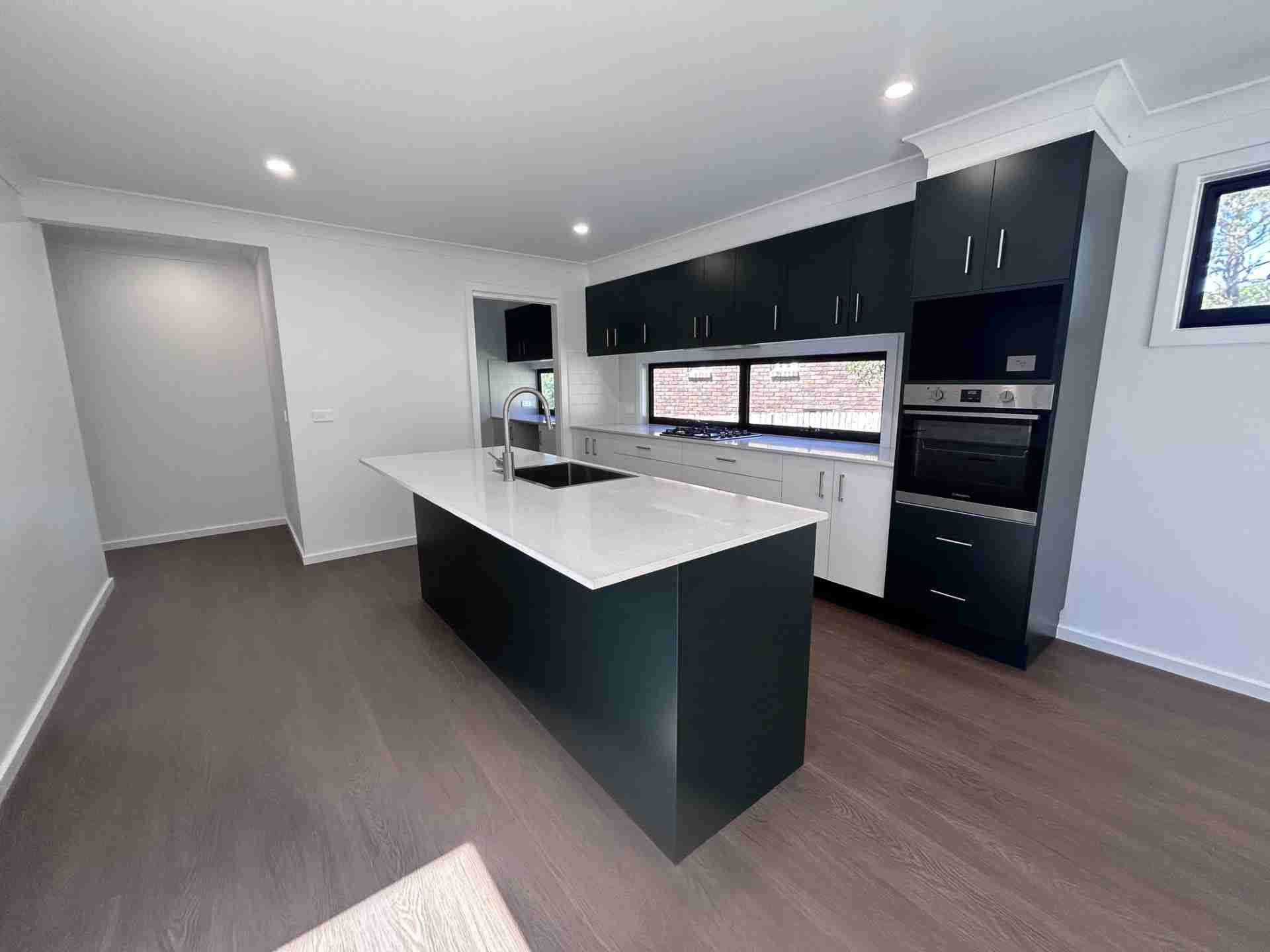 Modern kitchen with white island, black cabinets, wood floors, and recessed lighting