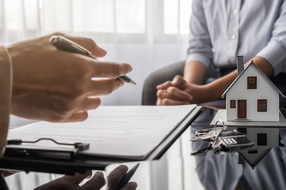 Hands signing real estate paperwork beside a small house model on a desk