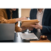Two people exchanging a folder over a desk with a laptop and gavel in a meeting room