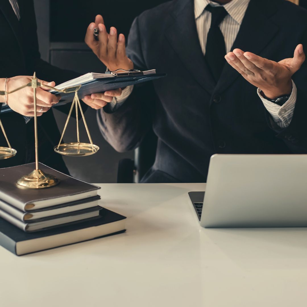Lawyers discussing justice at a desk with scales, a gavel, books, and a laptop