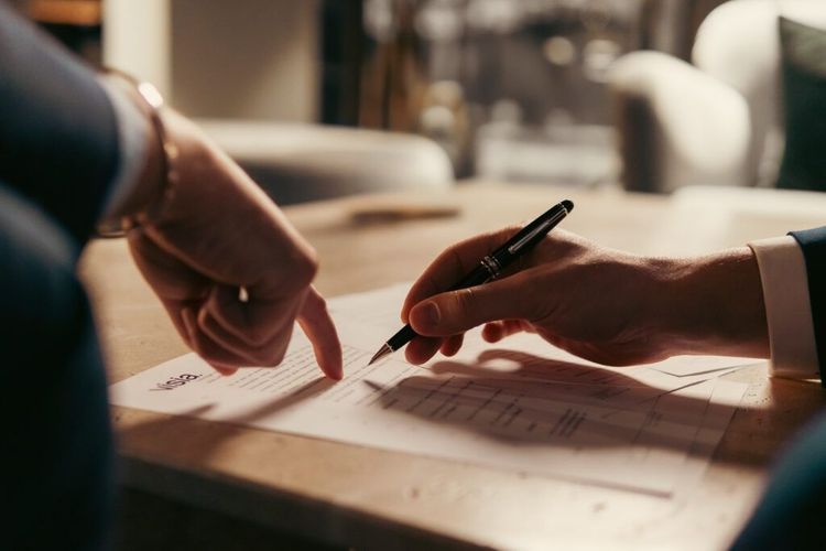 Two hands point and write on a document on a table in warm light