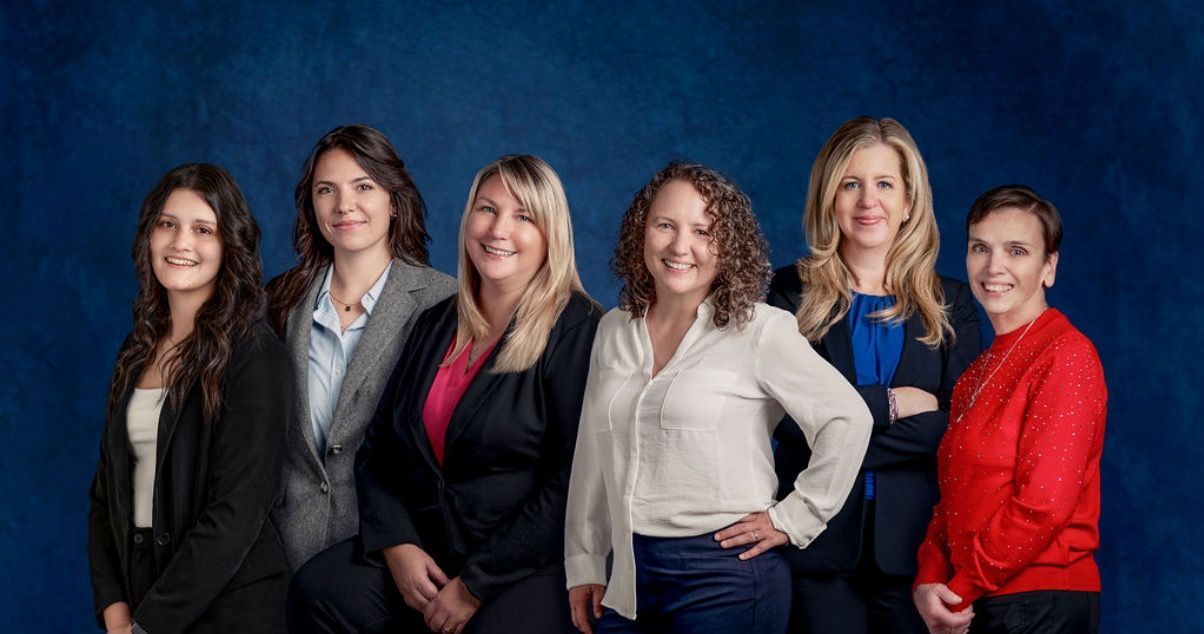 Four people posing in business attire against a blue studio backdrop