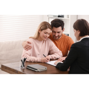 Couple signing documents with a counselor at a desk in a bright office