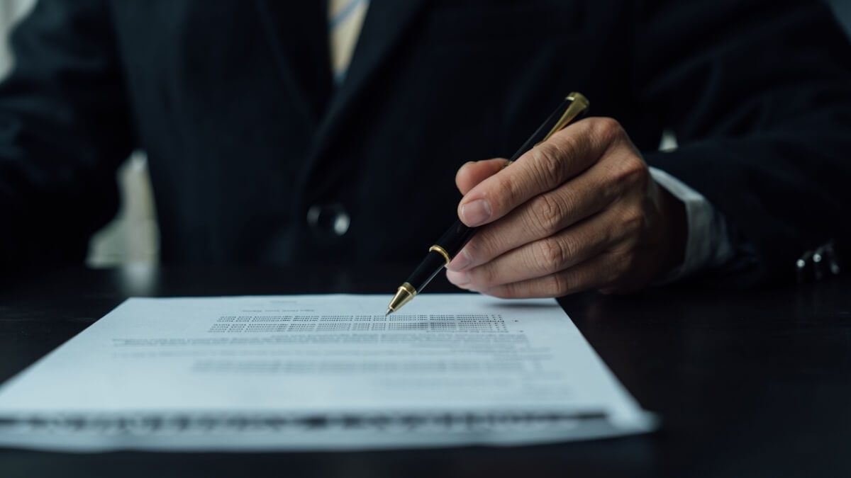 Hand signing a document on a desk with a pen
