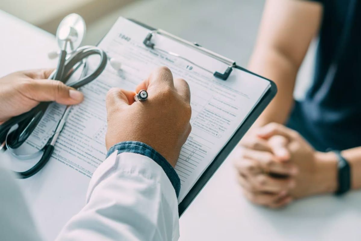 Doctor reviewing clipboard while talking with patient in a clinic, with stethoscope visible