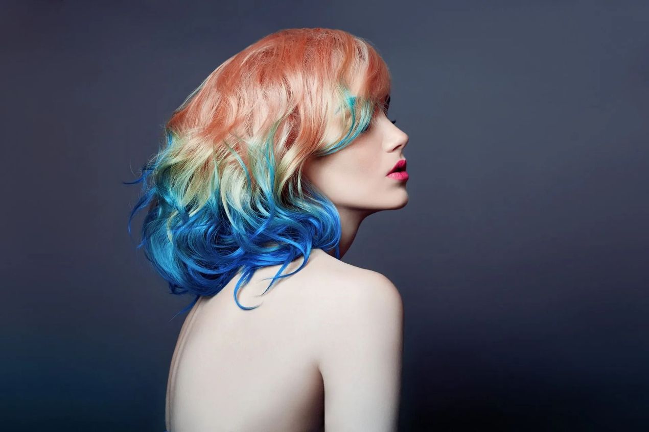 Ritratto del profilo di una persona con i capelli sfumati dal rosso al blu su uno sfondo scuro