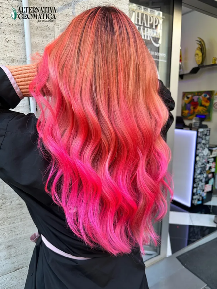 Capelli mossi rosa con sfumatura ombré e radici corallo, ripresi da dietro in un salone di bellezza