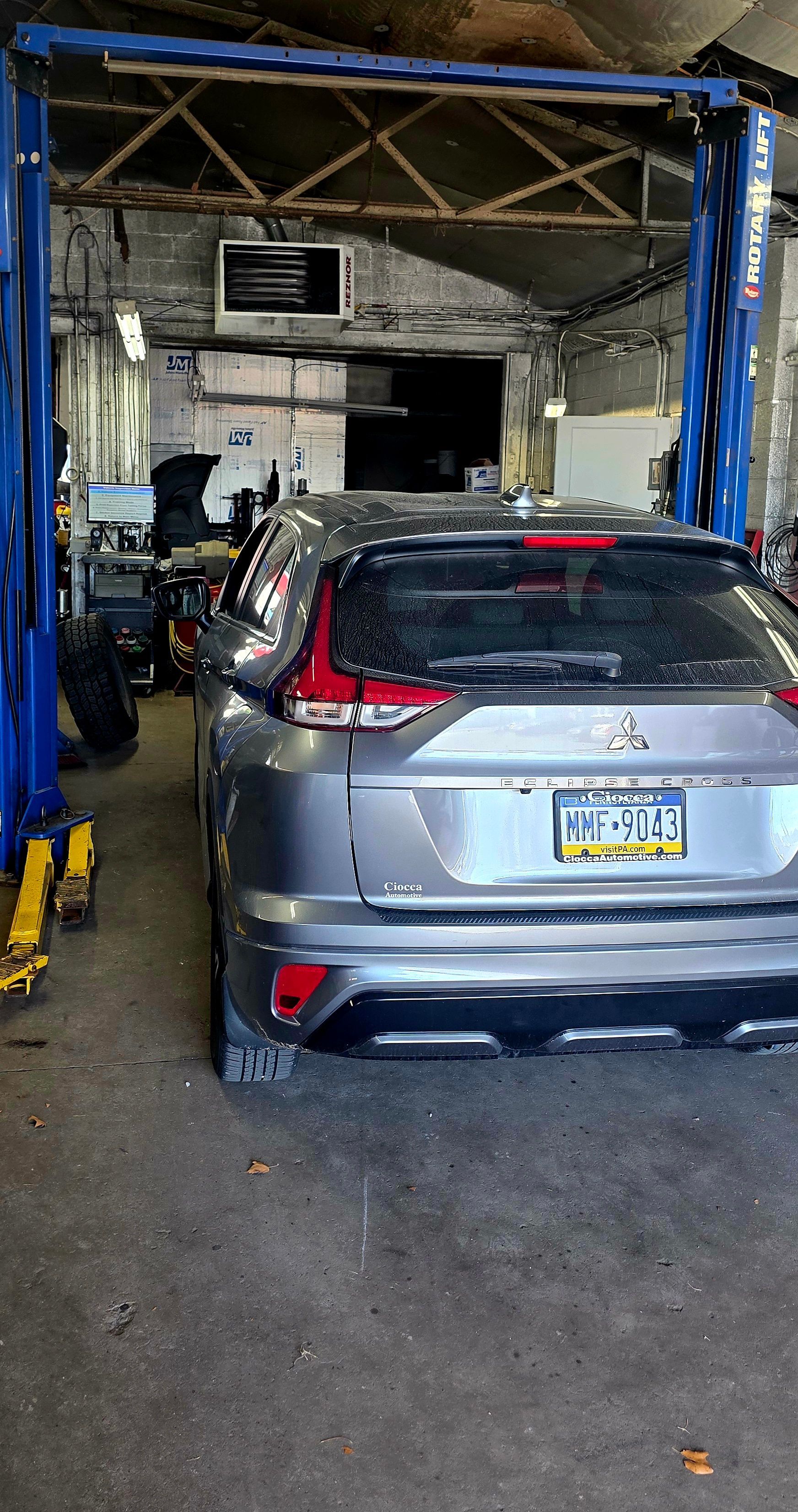 A grey Nissan Eclipse Cross SUV parked inside an auto repair shop between the metal columns of a vehicle lift.