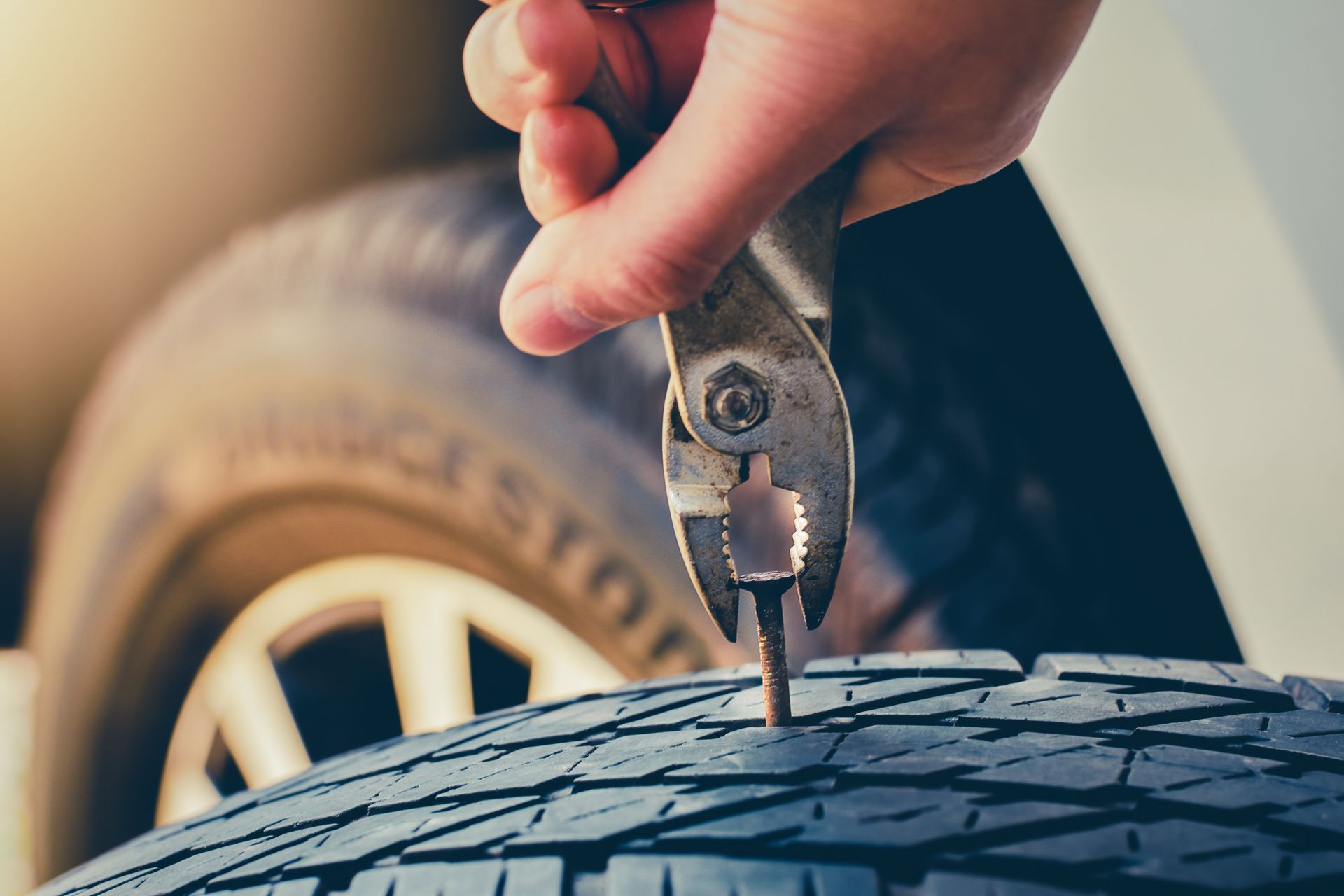 Hand using pliers to pull a nail out of a car tire tread.