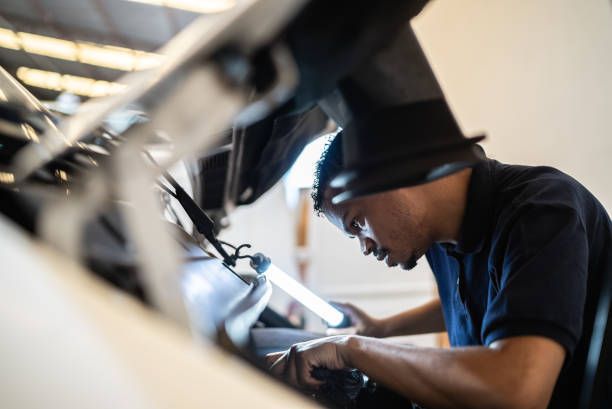 Auto repair technician checks a car engine with a blue light, with the car’s hood up.
