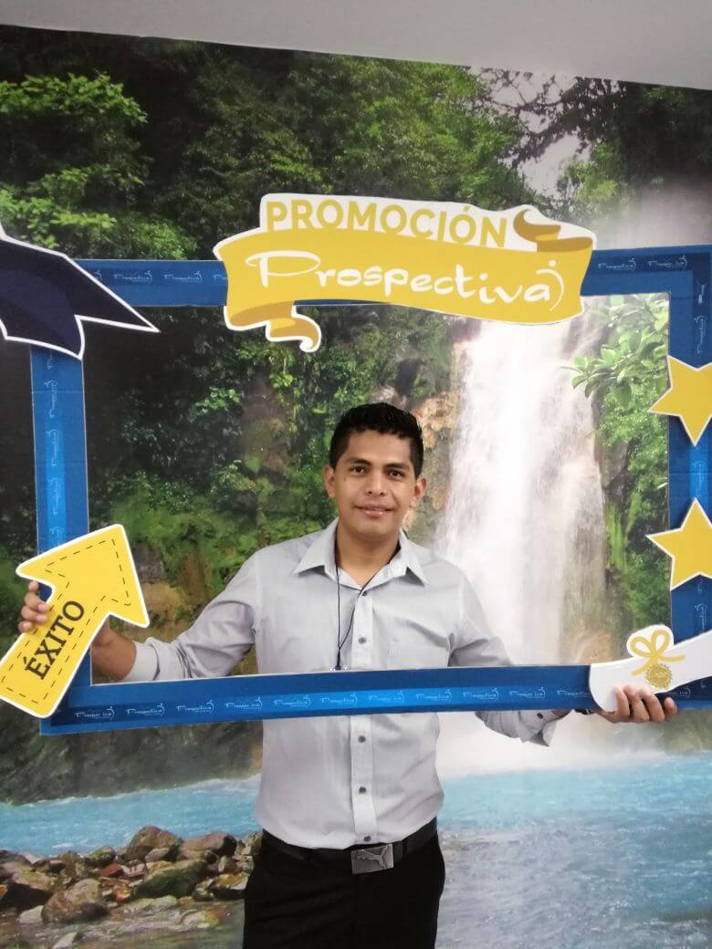 Hombre sosteniendo un marco promocional azul con la etiqueta “Prospectiva”, con una cascada de fondo y recortes de estrellas amarillas.