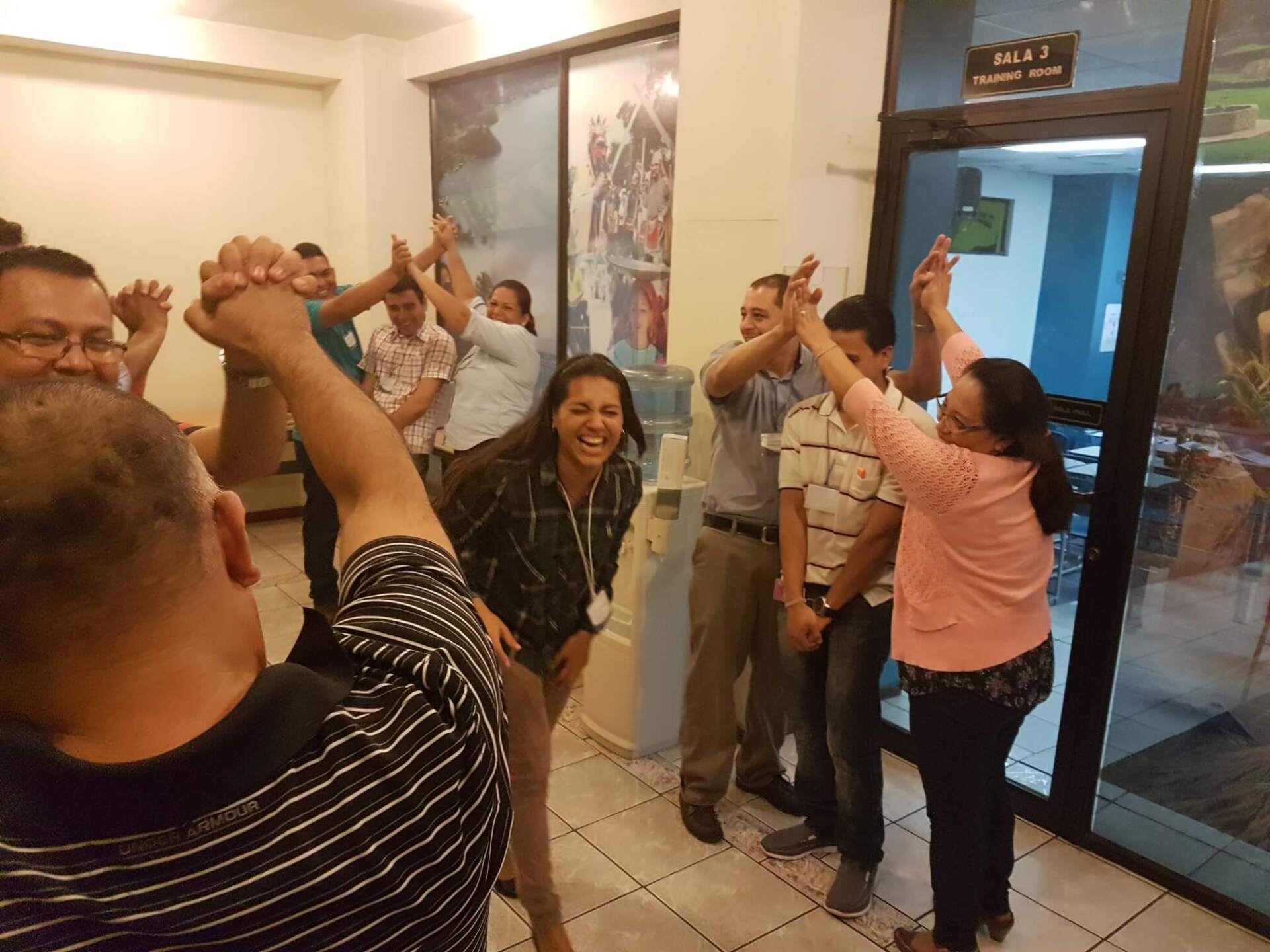 Personas tomadas de la mano en un pasillo, sonriendo y levantando los brazos juntos en señal de celebración.