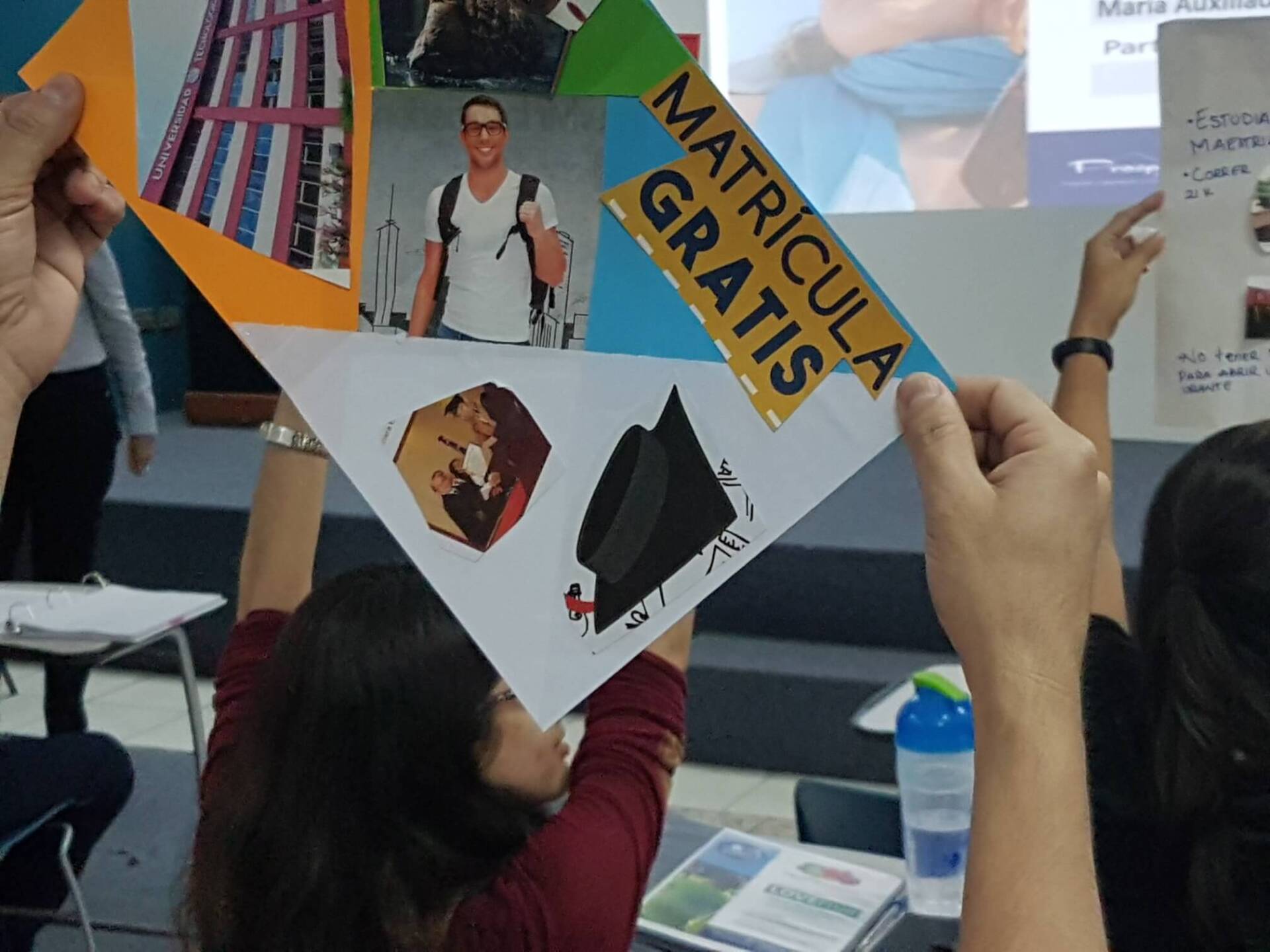 Personas sosteniendo un colorido cartel de “MATRICULA GRATIS” en un stand de un evento en el interior.