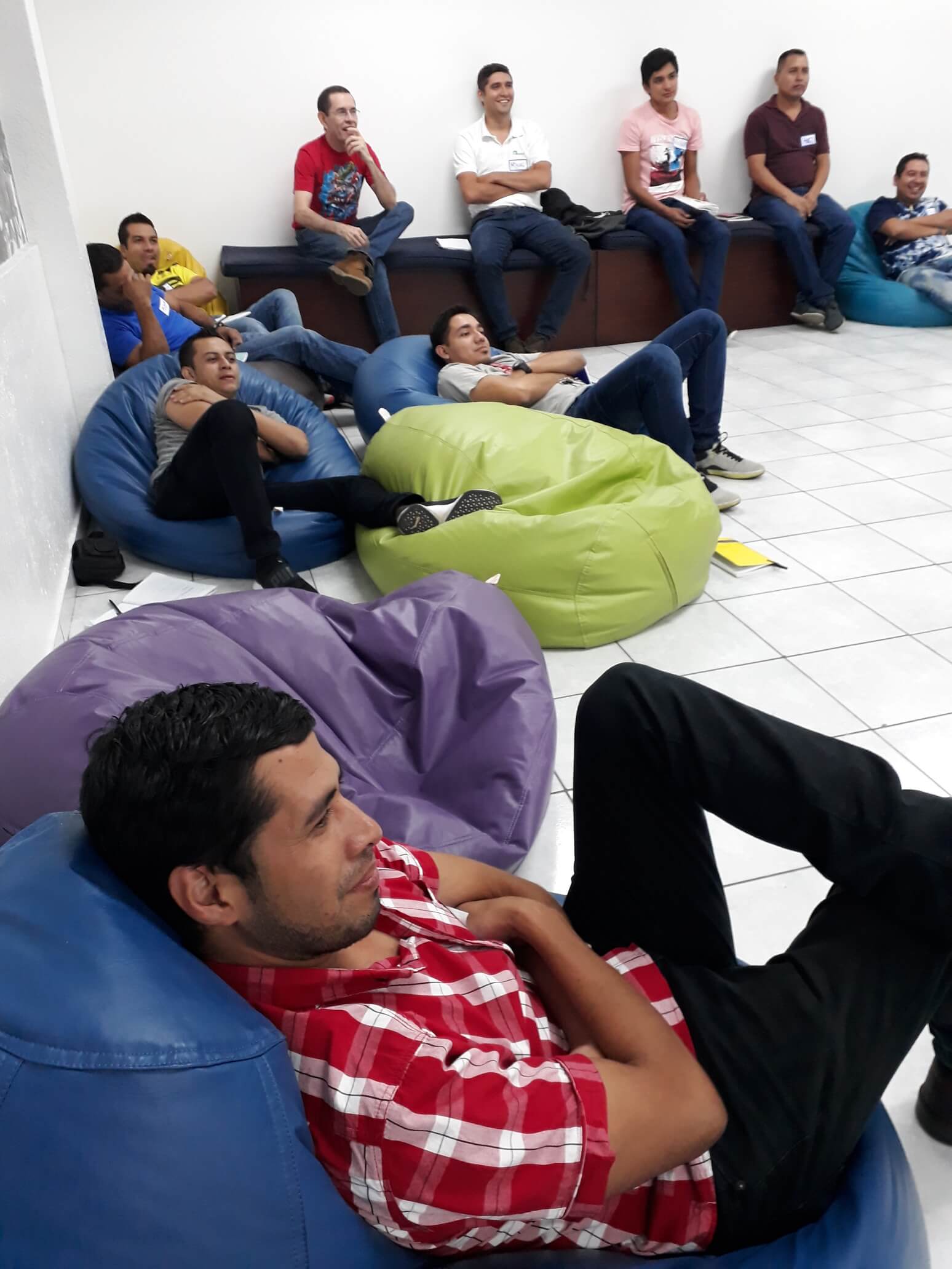 Gente relajándose en pufs en un salón, sentada y reclinada sobre cojines azules, verdes y morados.