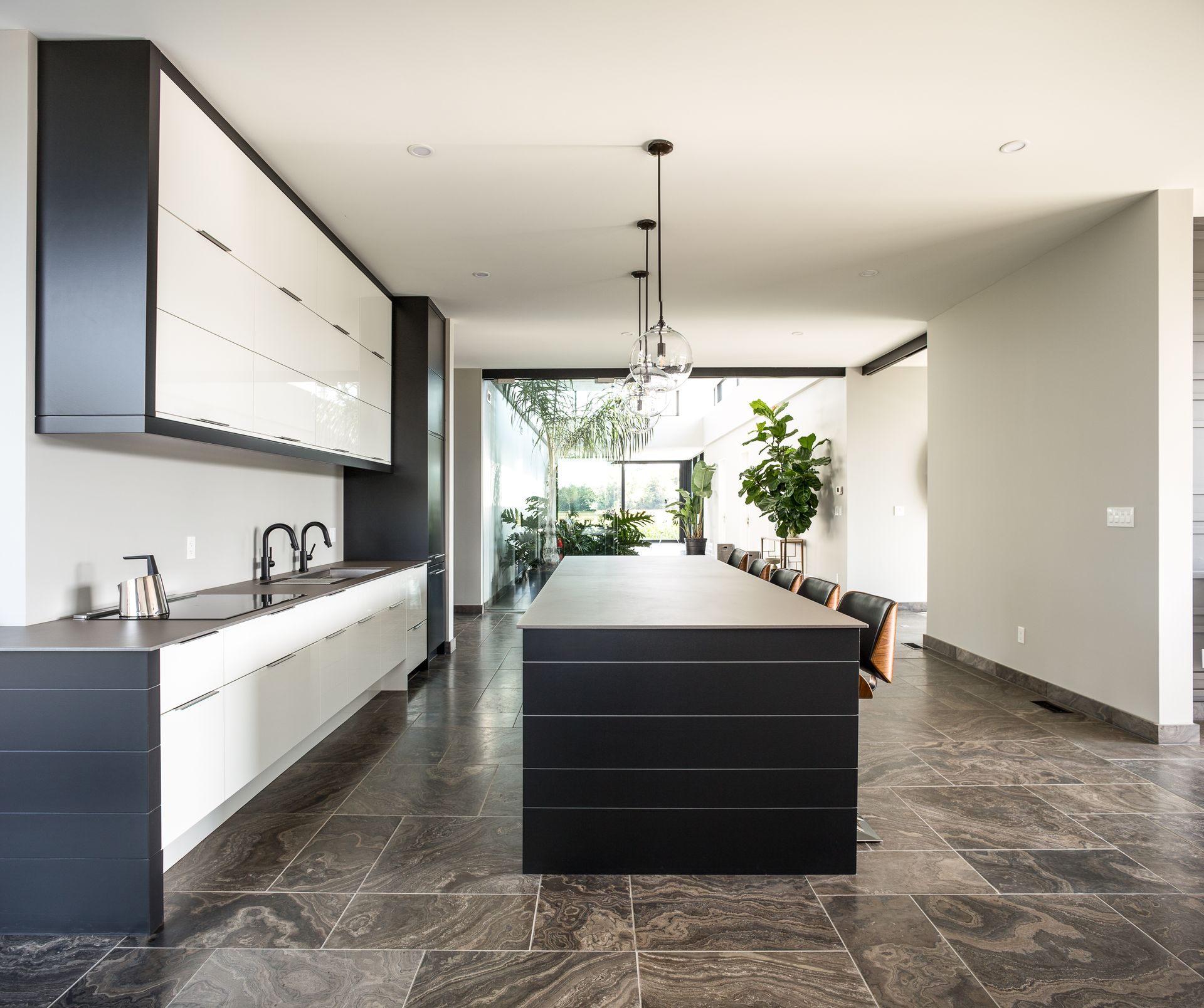 Modern kitchen with black and white cabinetry, a large island, and stone flooring.