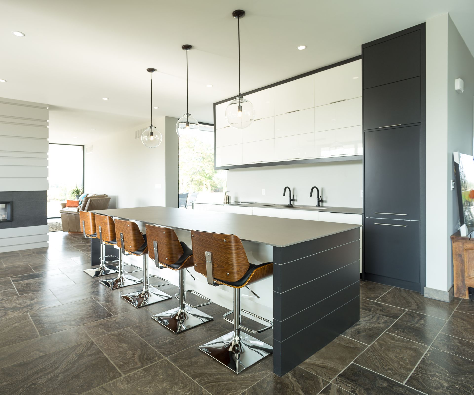 Modern kitchen with island, stainless steel countertop, and wooden barstools. White and dark gray cabinets, dark floor.