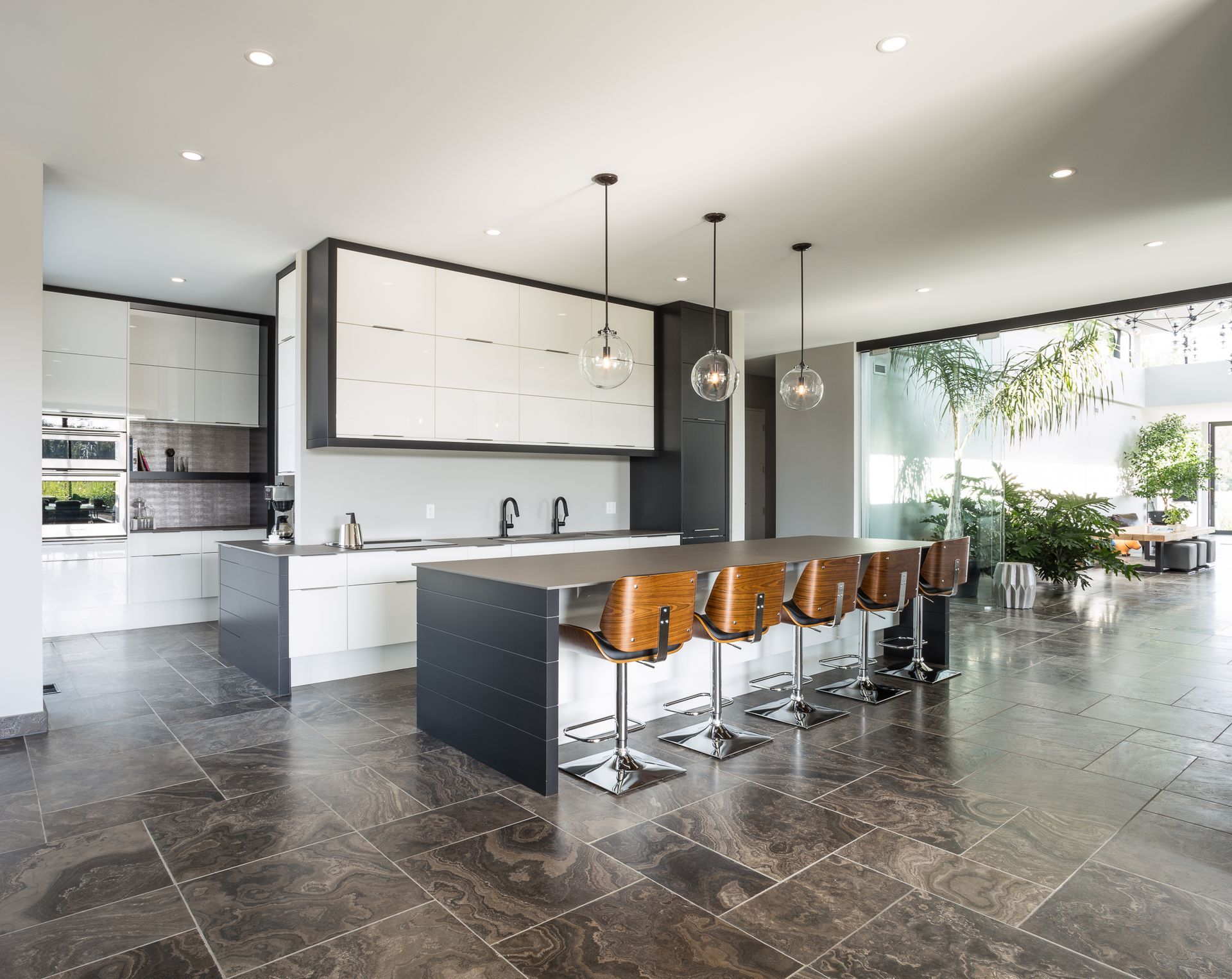 Modern kitchen with white and black cabinets, island with stools, dark tile floor, and large windows.