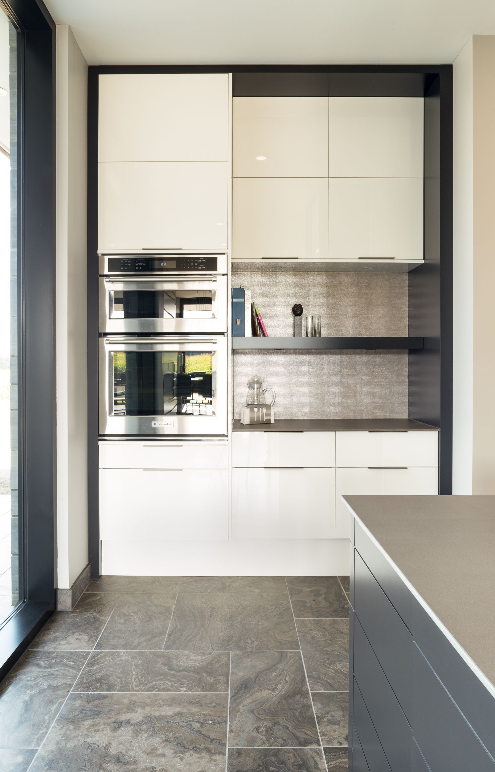 Modern kitchen with white cabinets, stainless steel ovens, and gray countertop.