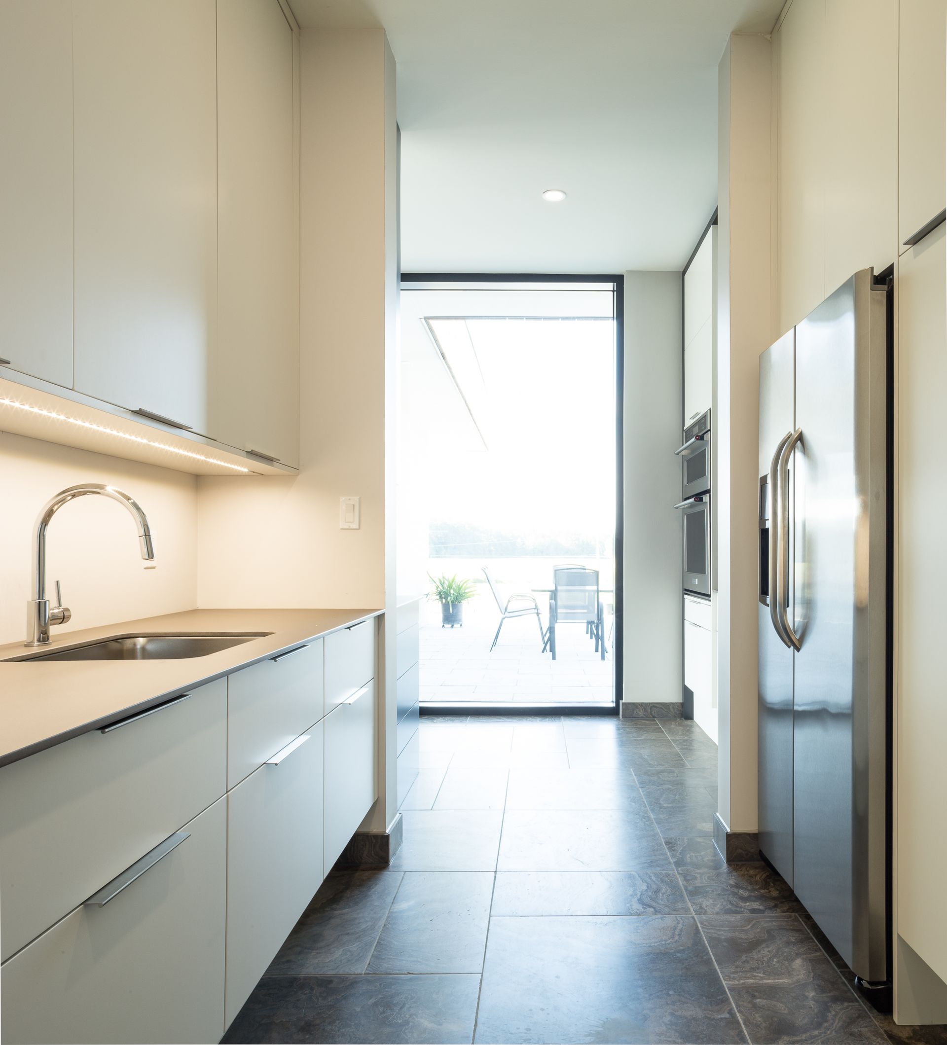 Modern kitchen with light cabinets, stainless steel appliances, and a view to an outdoor patio.