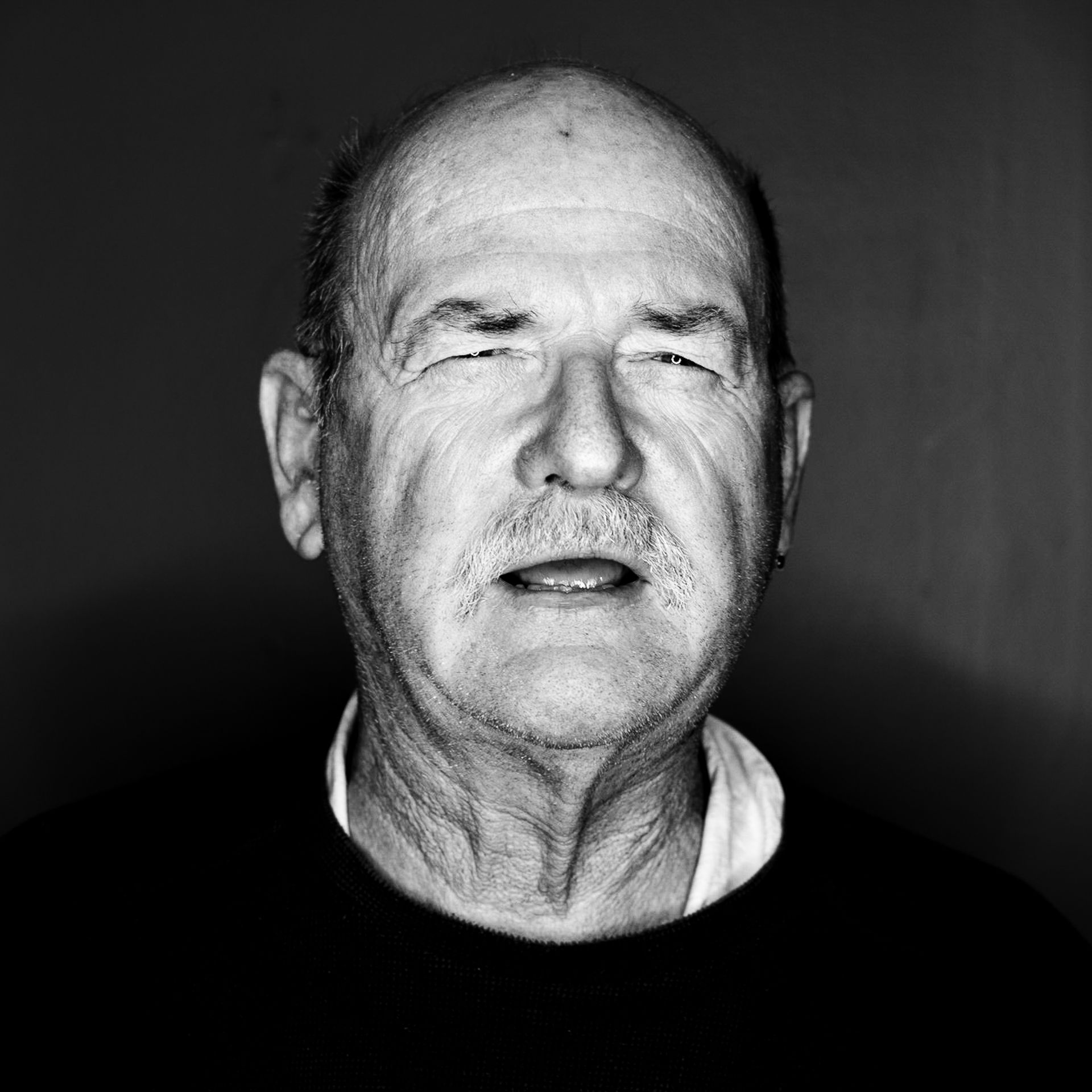 Close-up, black and white portrait of a man with a mustache, looking directly at the camera.