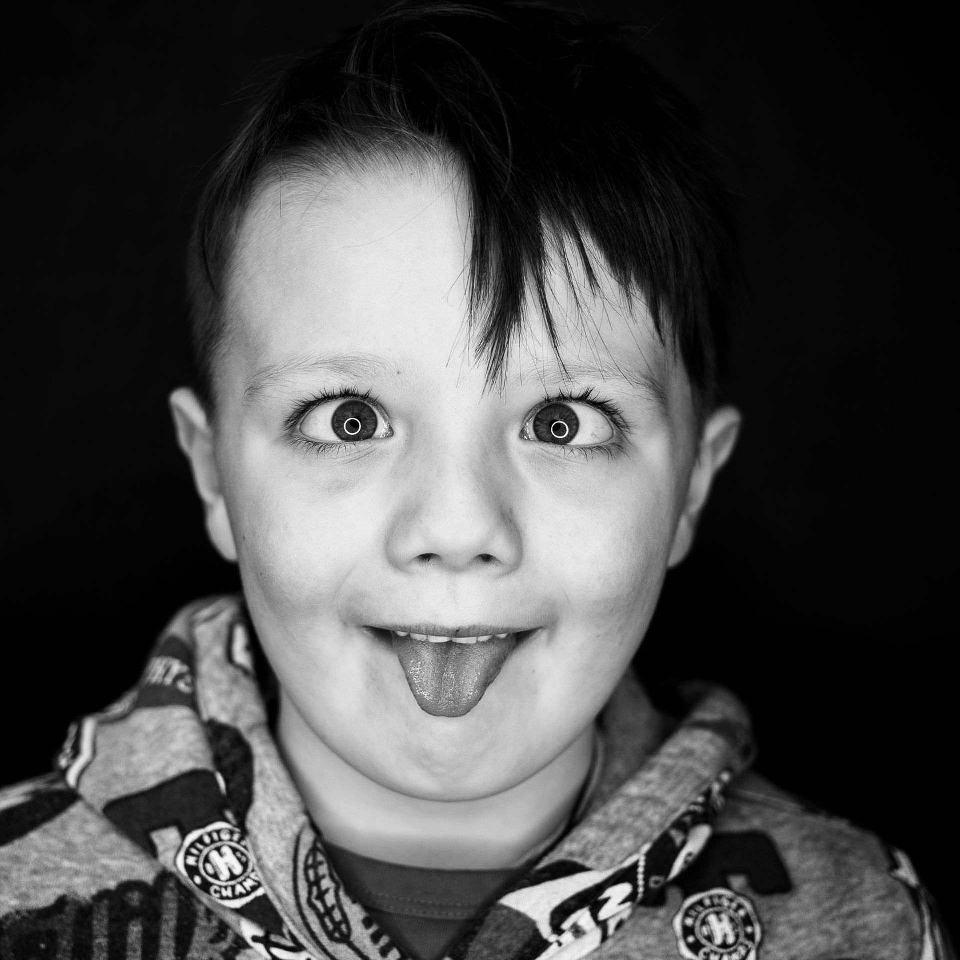 Child with crossed eyes and tongue sticking out, wearing a hooded sweatshirt.