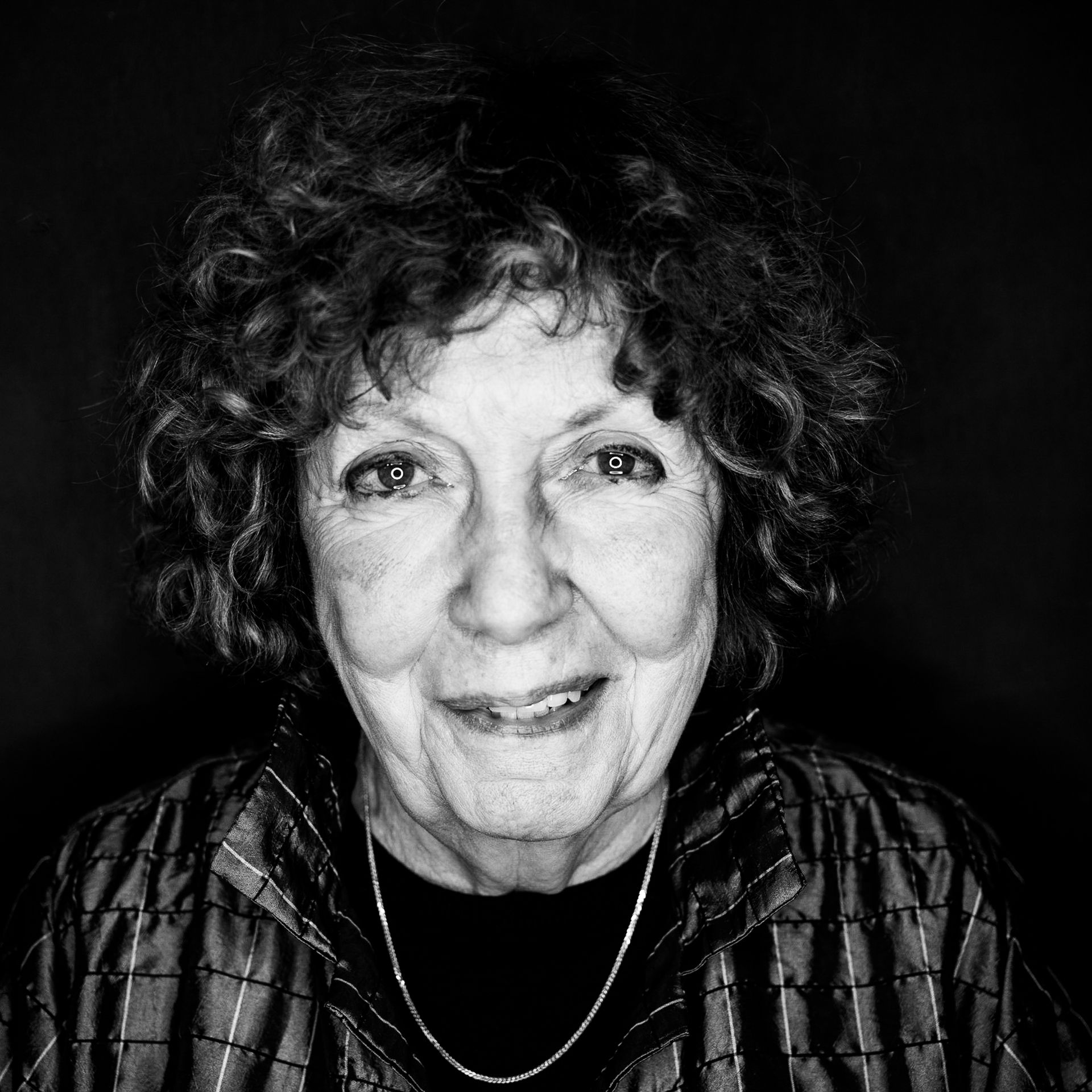 Woman with curly hair smiles, wearing a striped jacket and necklace. Black and white portrait.