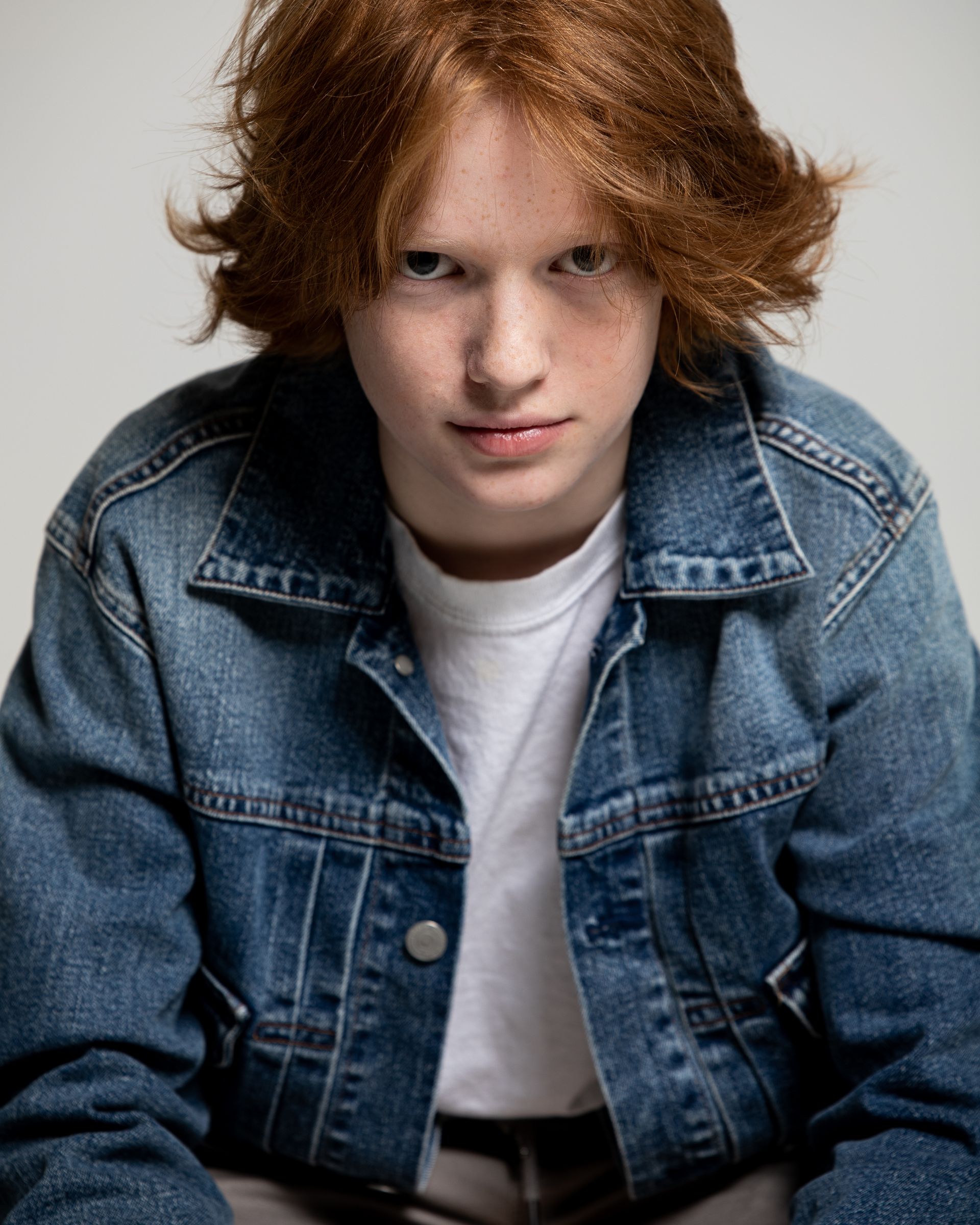 Person with red hair wearing a denim jacket, looking directly at the camera with a neutral expression.