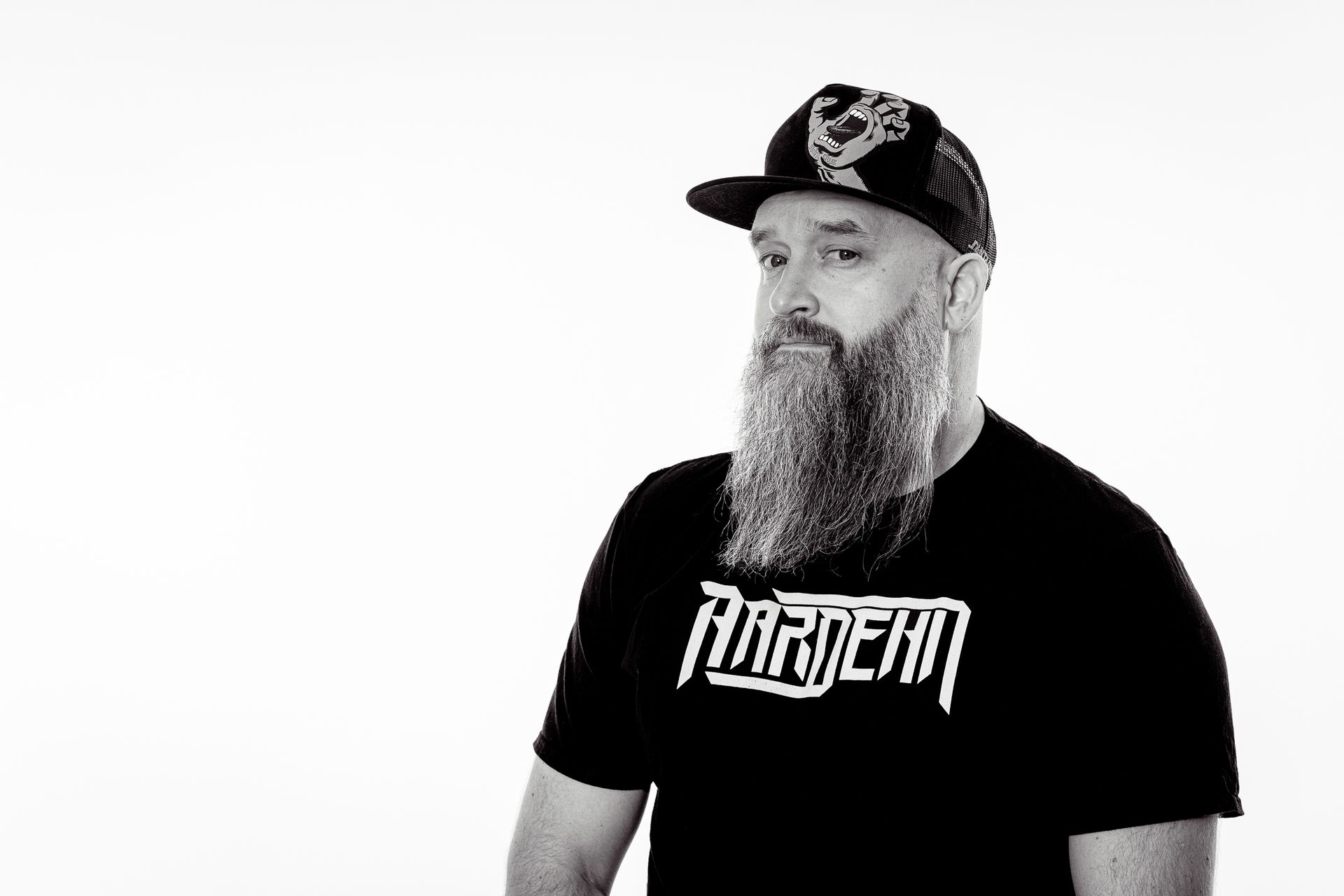 Man with a long beard and baseball cap, wearing a black t-shirt, looking to the side.