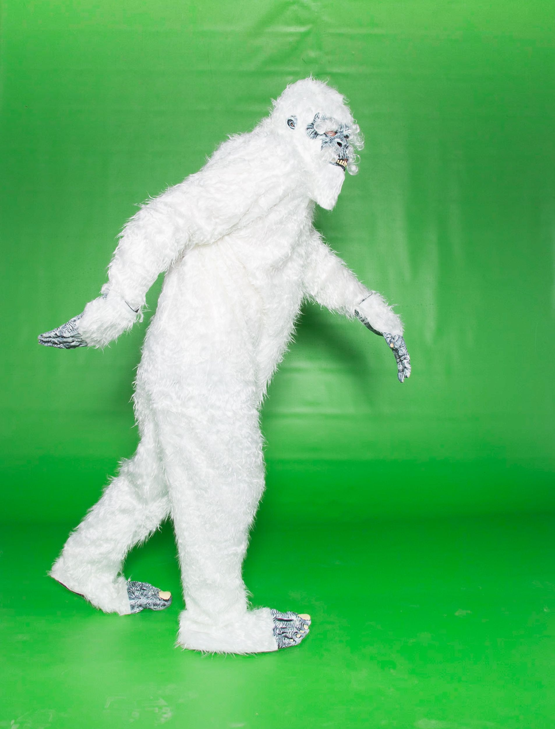 A person in a white Yeti costume walks right against a green background.