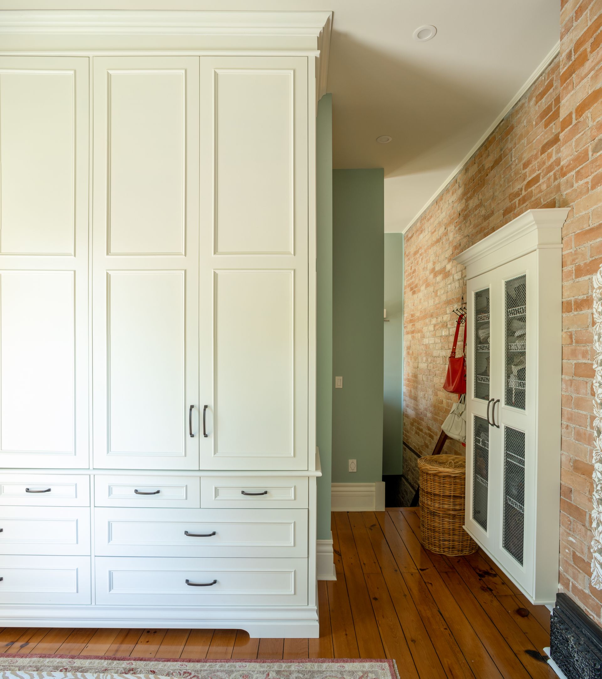 White built-in cabinets and drawers next to a brick wall hallway with hardwood floors.