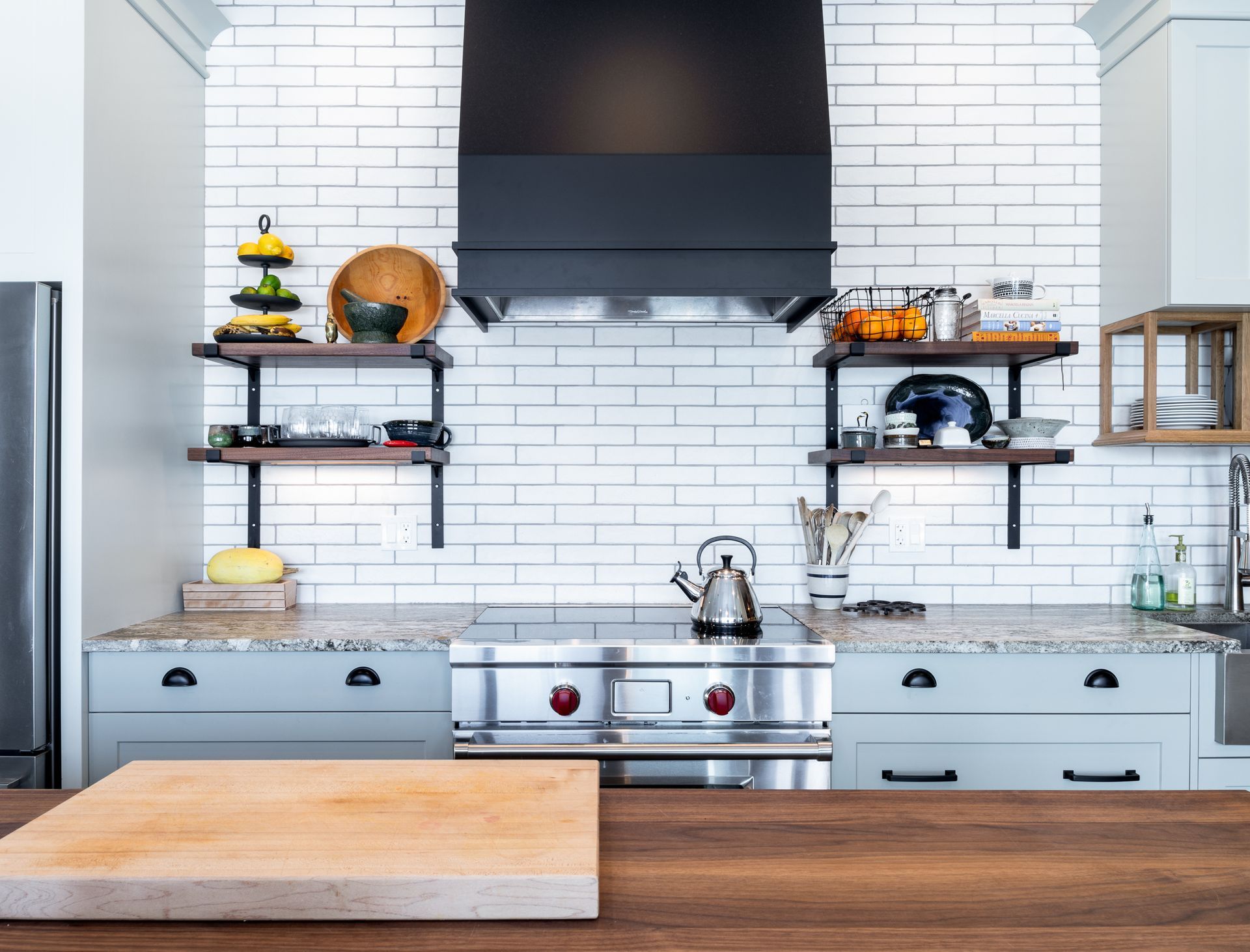 Kitchen with white brick backsplash, stainless steel range, and open shelving.