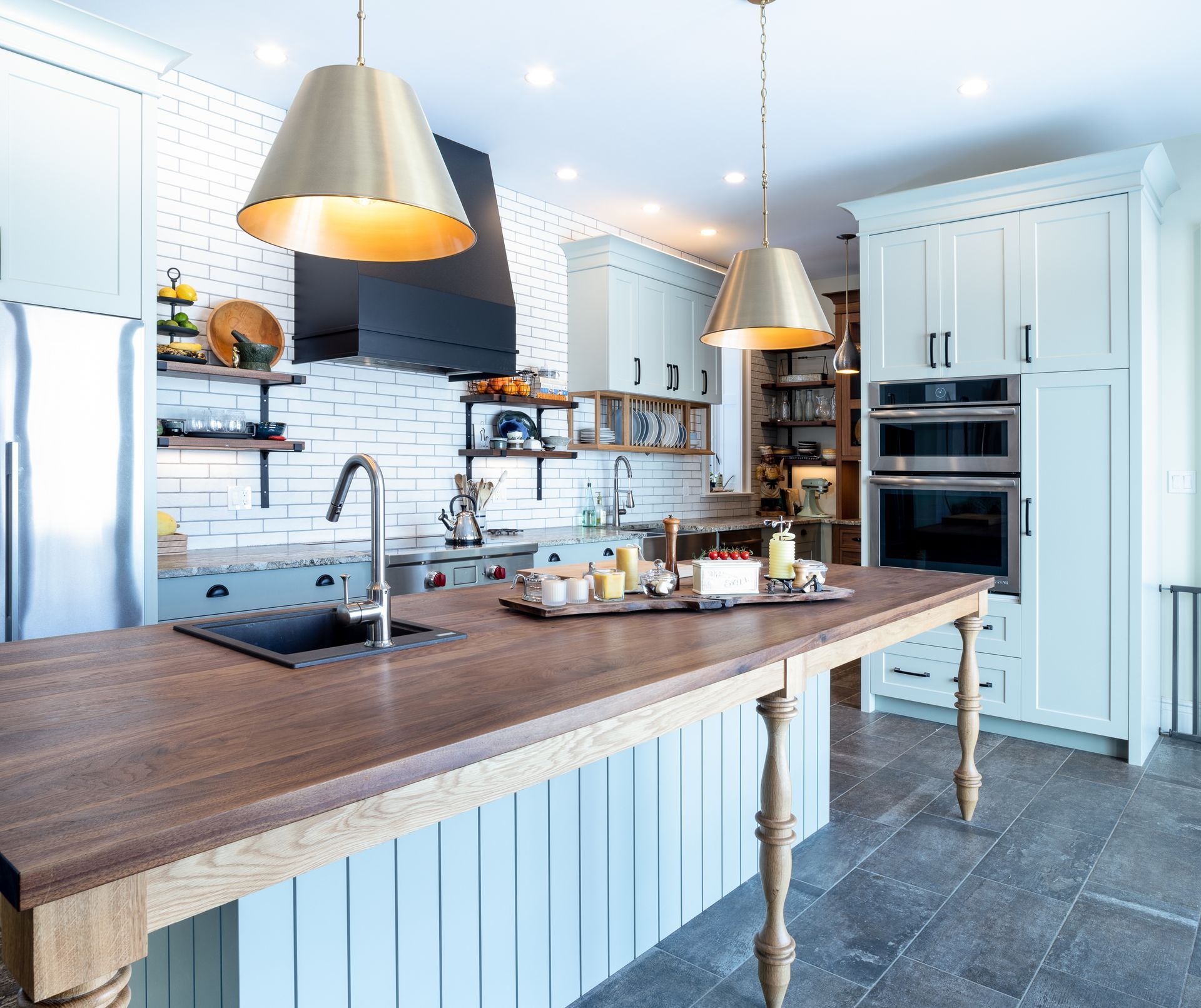 Kitchen with light blue cabinets, dark wood island, gold pendant lights, and brick backsplash.