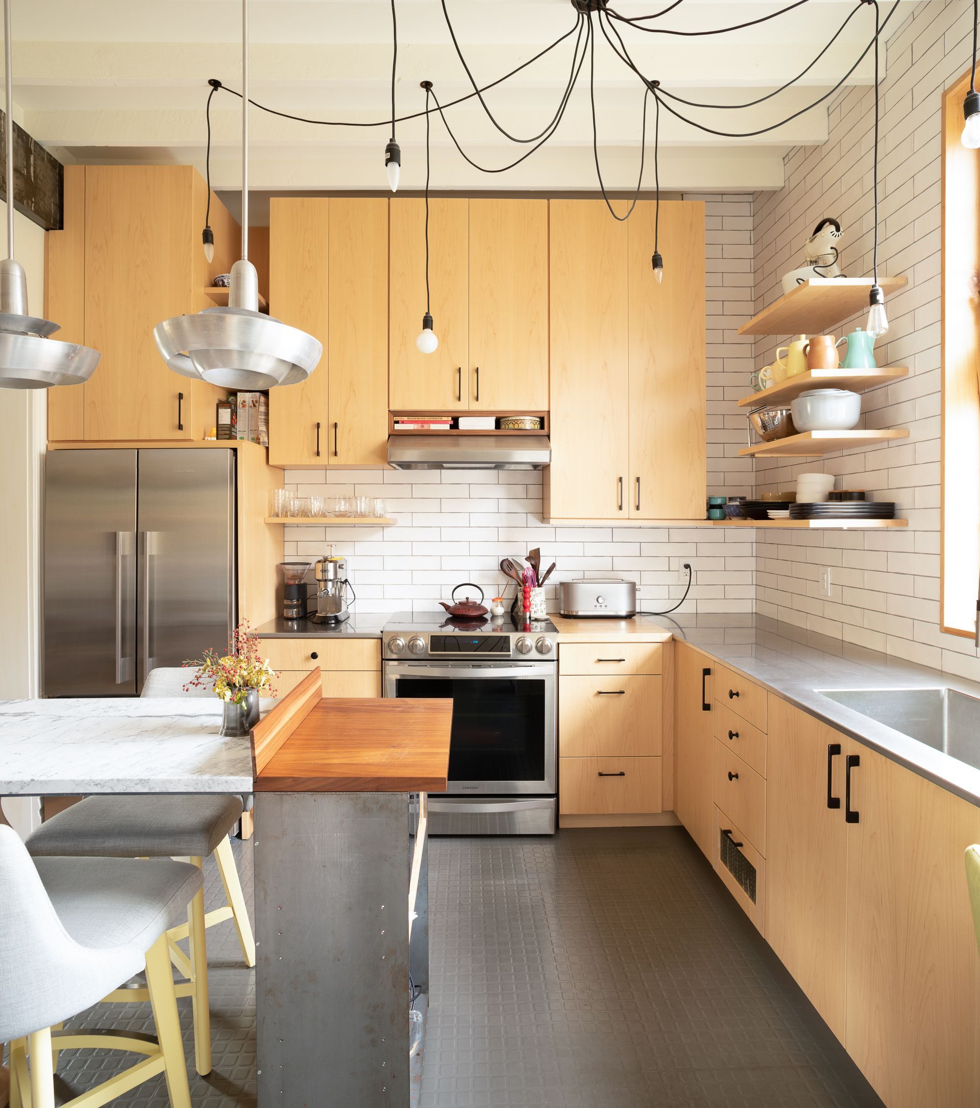 Modern kitchen with light wood cabinets, stainless steel appliances, and a gray concrete floor.