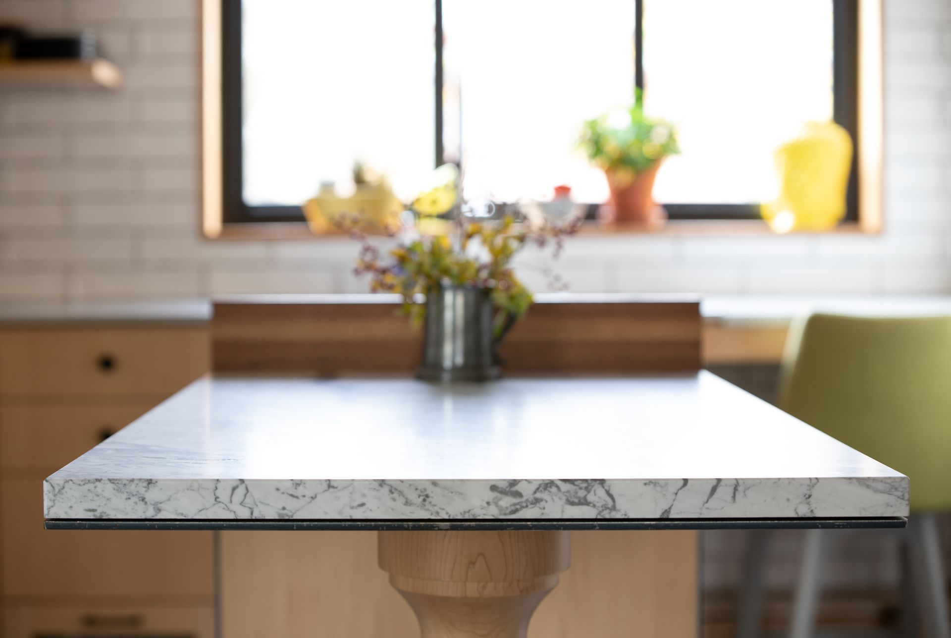 Kitchen island with marble countertop, wooden base, and flowers in front of a window.