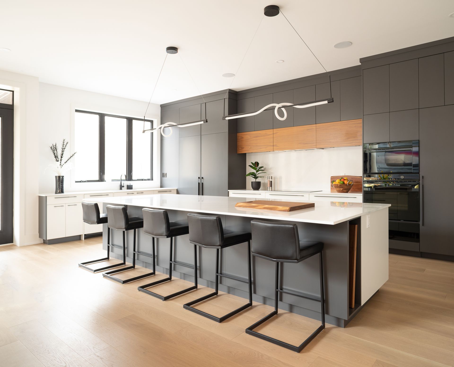 Modern kitchen with island, gray cabinets, white countertops, black bar stools, and linear lighting.