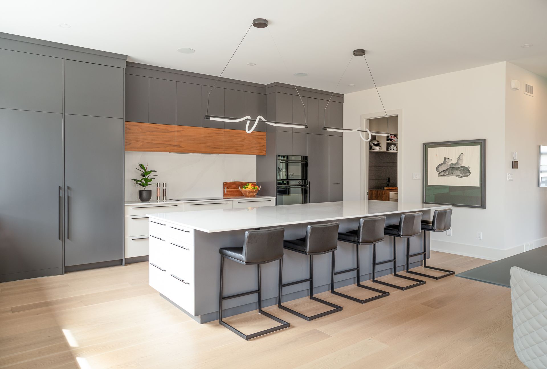 Modern kitchen with gray cabinets, white countertop island, bar stools, wood accents.