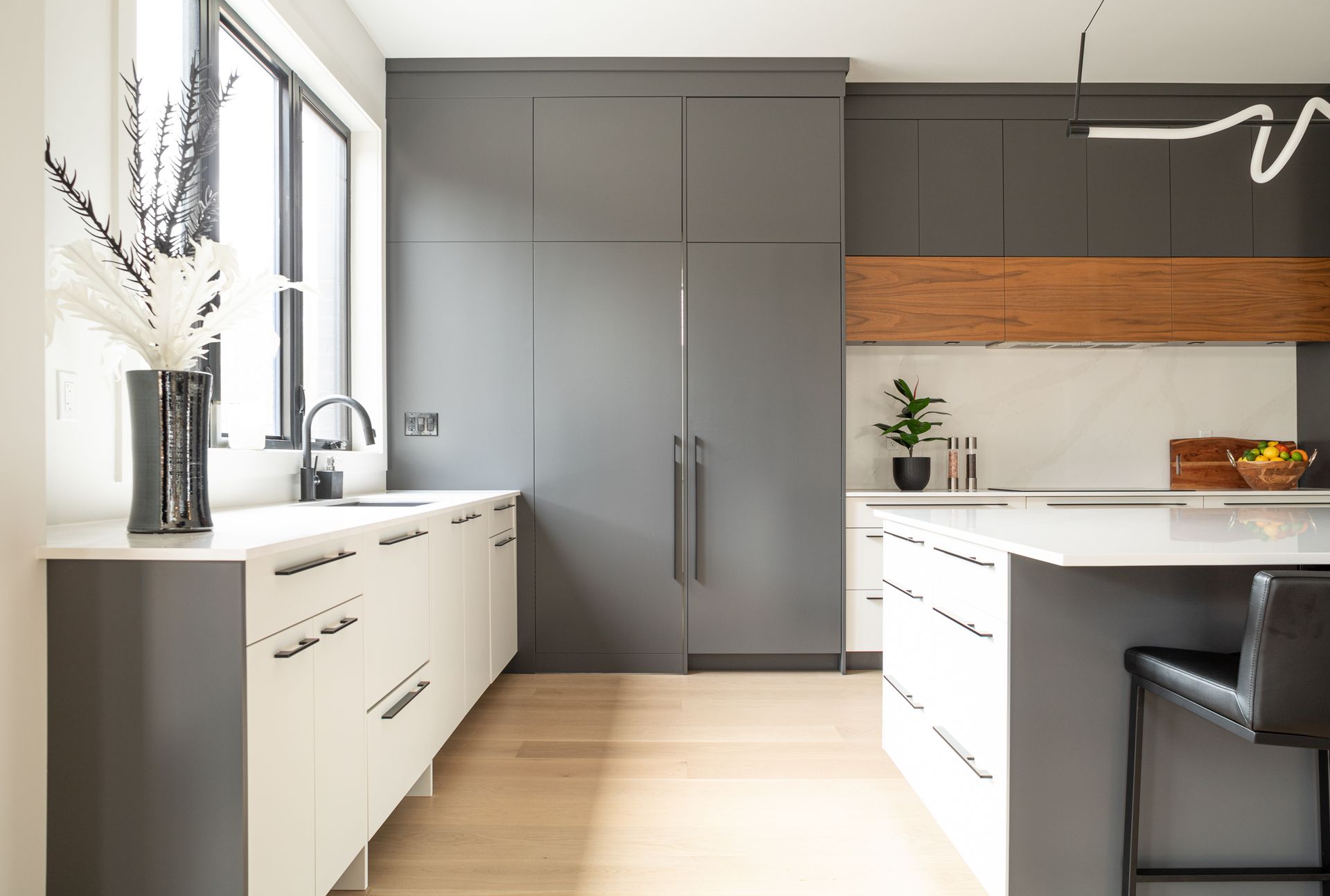 Modern kitchen with gray and white cabinets, wood accents, and a large window.
